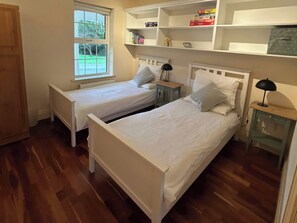 A room with two single beds, a window, a bookshelf, and a bedside table with a lamp. - The Sanctuary (Churchfield)