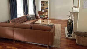 Un salon avec un canapé en cuir marron, une table basse, une bibliothèque, une cheminée et un miroir.