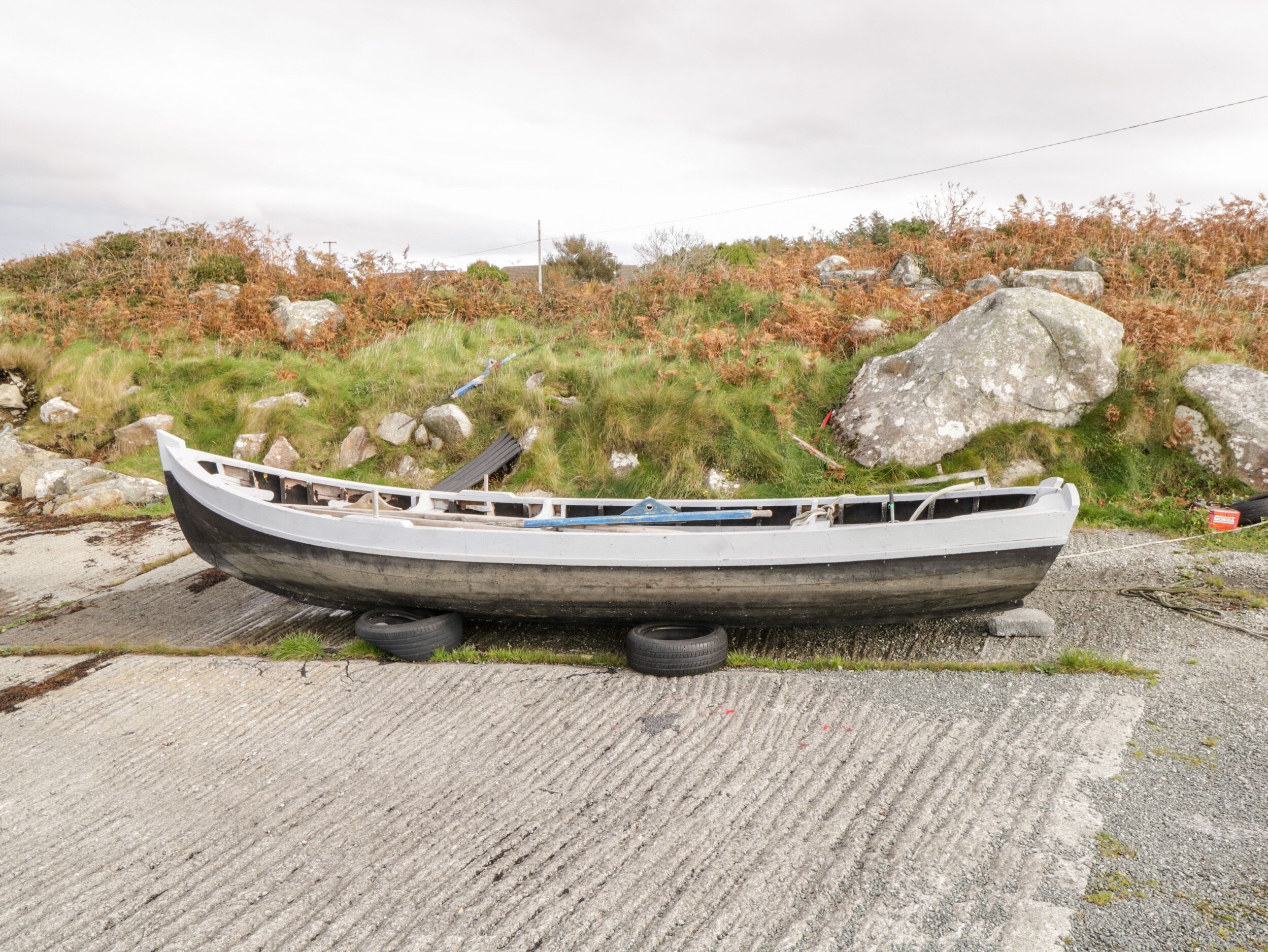 A boat parked on a concrete surface with grass and rocks in the background.