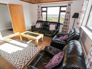 A living room with a sofa, a coffee table, and a view of a river. - Aras Iosgan (Carraroe)