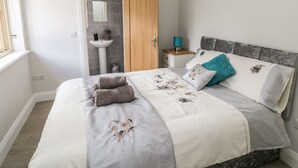 Un dormitorio con cama, mesita de noche, ventana y baño con lavabo y espejo.