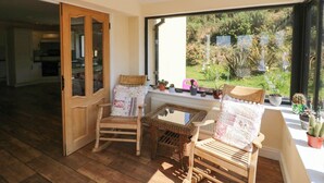 Una stanza luminosa con pavimento in legno, una sedia in vimini, una poltrona imbottita e una finestra vista giardino.
