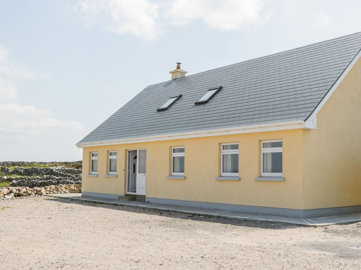 A single-story house with a grey roof, a small porch, and a gravel driveway.