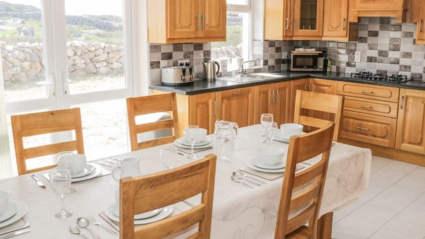 Una cocina moderna con armarios de madera, salpicadero de azulejos y una zona de comedor preparada para seis personas.