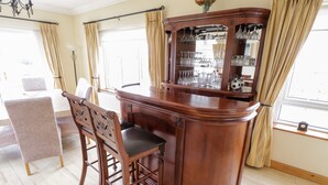A bar area with a wooden bar counter, chairs, and a glass display cabinet with various glassware.