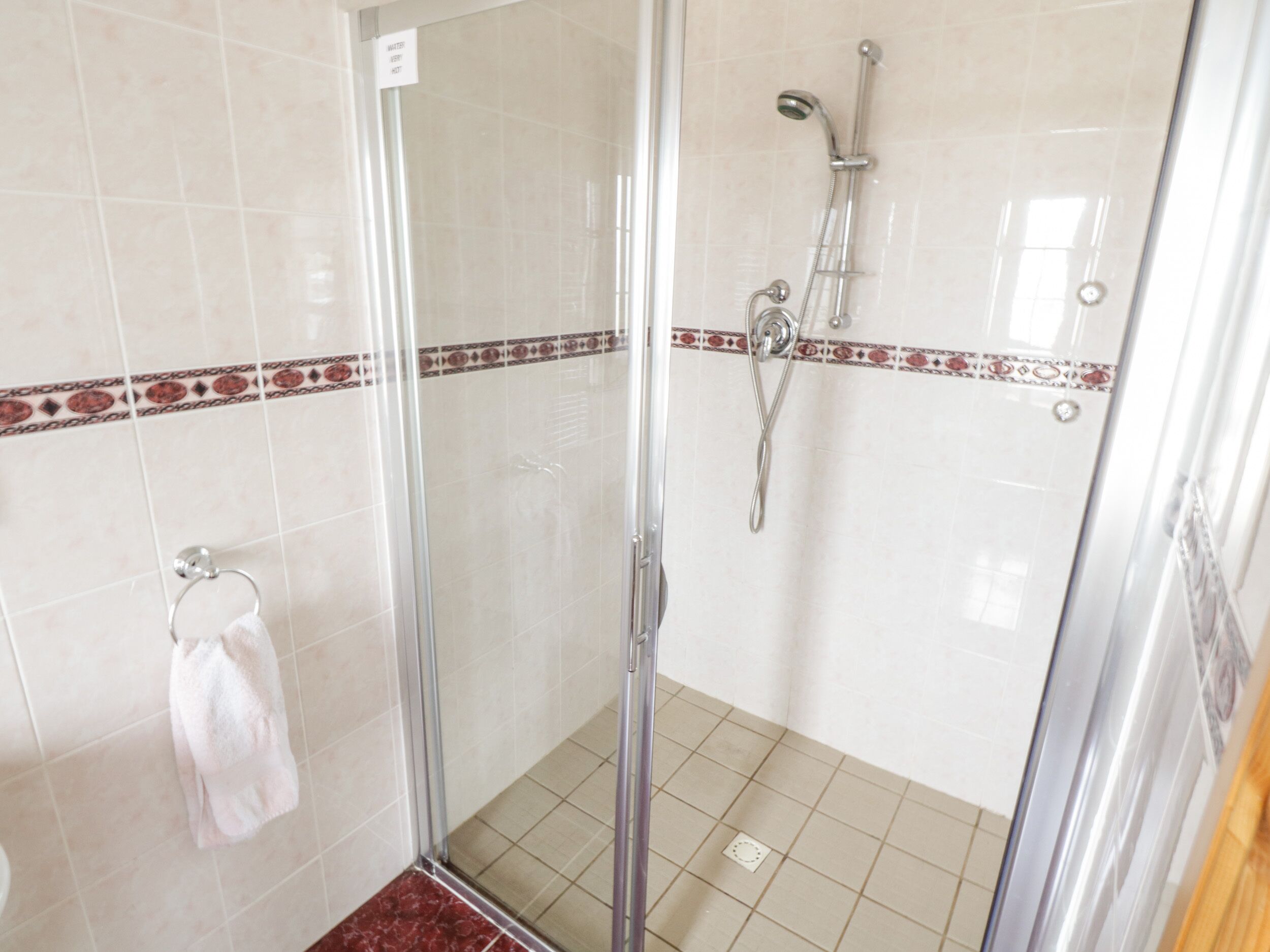 A glass-enclosed shower area with a handheld showerhead and a wall-mounted faucet.