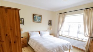 A bedroom with a large bed, wooden wardrobe, and a window with curtains.