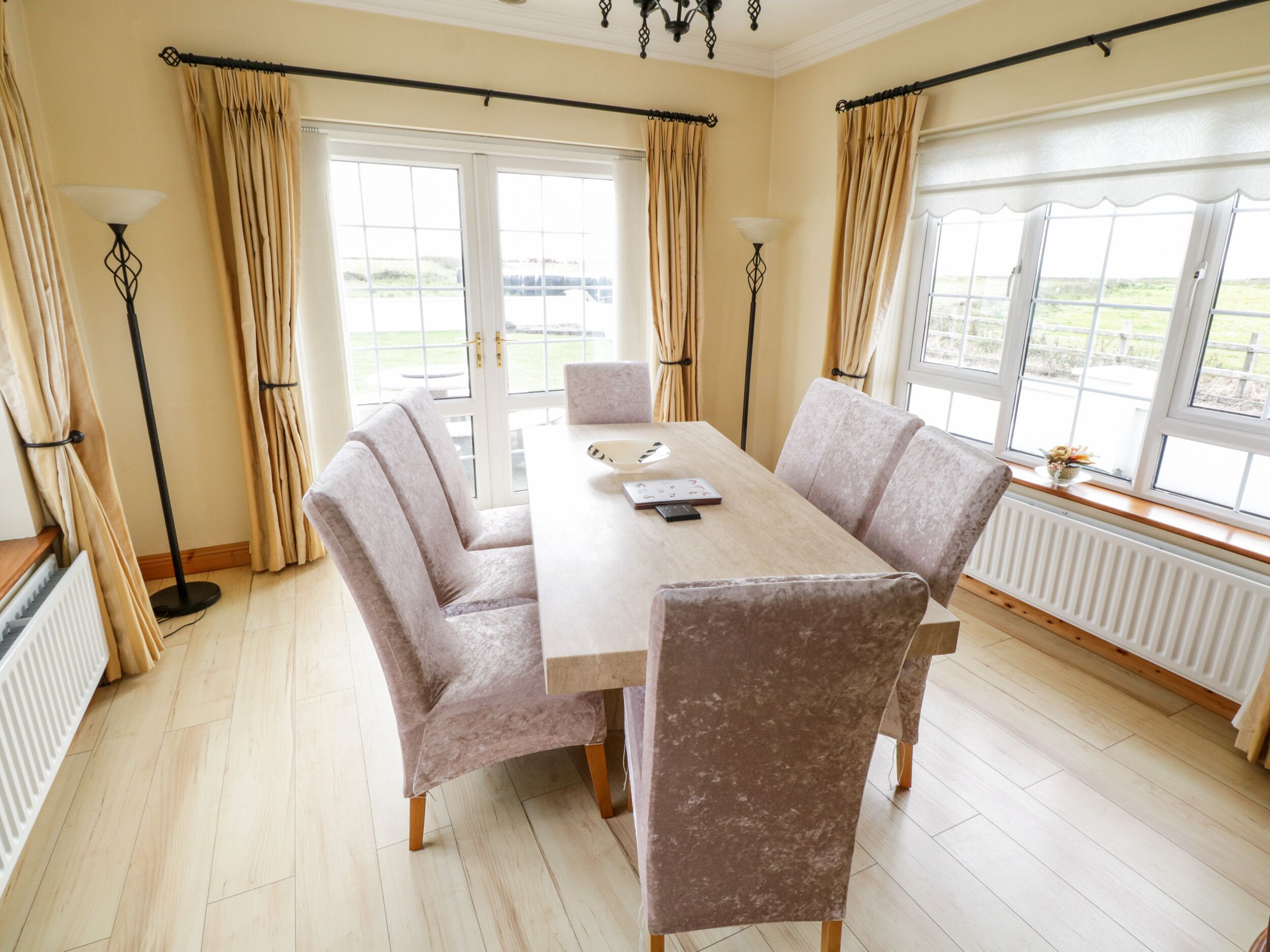 Ein Esszimmer mit großem Tisch, vier Stühlen und Blick ins Freie durch große Fenster.