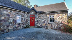 A stone house with a red door, two windows, and a gravel driveway. - Rose Cottage (Ramsgrange)