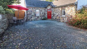 A stone house with a red door, a gravel driveway, and a red umbrella. - Rose Cottage (Ramsgrange)