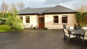 Une maison à deux étages avec une porte d’entrée, des fenêtres et un patio comprenant une table et des chaises.