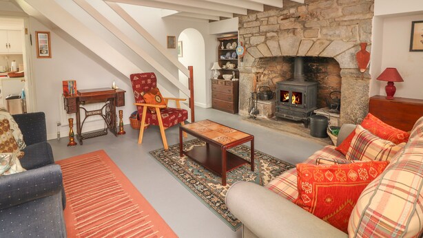 A cozy living room with a stone fireplace, a wooden chair, a sofa, and a dining table. - Limestone Cottage (Carran)