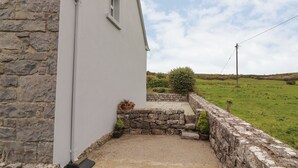 A stone building with a small window and a paved entrance area with potted plants. - Limestone Cottage (Carran)