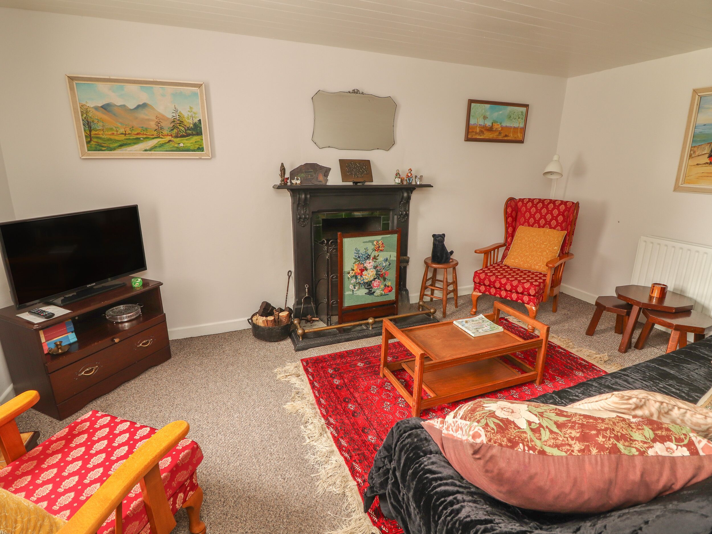 A living room with a fireplace, a television, a red patterned armchair, a wooden coffee table, and a red carpet.