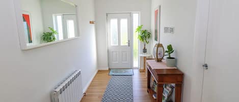 Un pasillo con un radiador, un tapete estampado, un banco de madera con revistas y una puerta con un panel de vidrio.