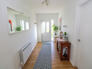 A hallway with a radiator, a patterned rug, a wooden bench with magazines, and a door with a glass panel. - 2 Castle Cove (Dromahair)