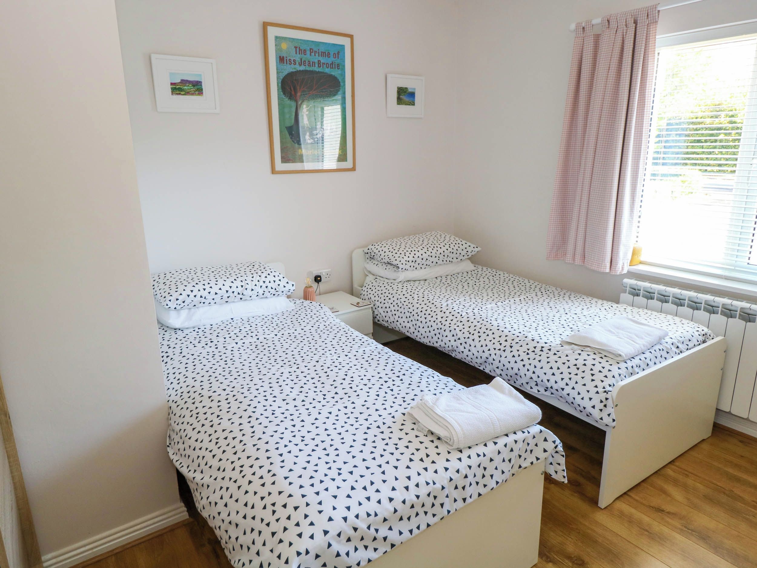 A bedroom with two single beds, a radiator, a window with curtains, and a framed picture on the wall.