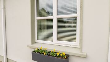 A window with blinds and a planter box with flowers.