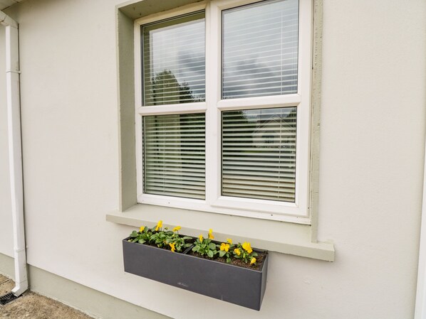 A window with blinds and a planter box with flowers. - 2 Castle Cove (Dromahair)