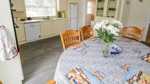A dining area with a round table covered in a patterned tablecloth, surrounded by wooden chairs. - 2 Castle Cove (Dromahair)
