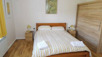 Una cama bien hecha con ropa de cama a rayas, dos lámparas de noche, un cabecero de madera, un armario de madera y un cuadro en la pared.