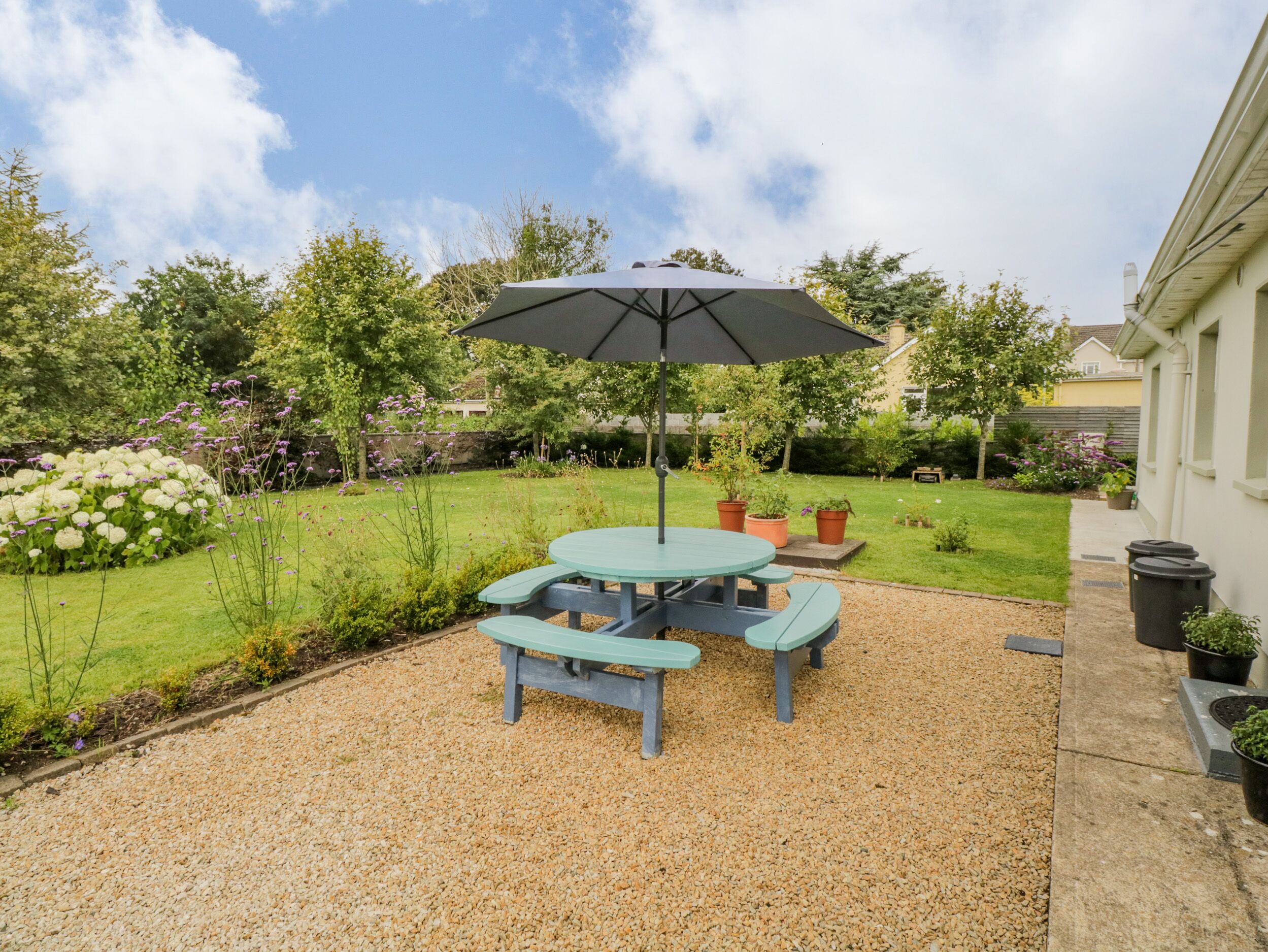 A patio with a table and benches, surrounded by gravel, under a large umbrella.