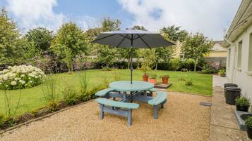 A patio with a table and benches, surrounded by gravel, under a large umbrella.