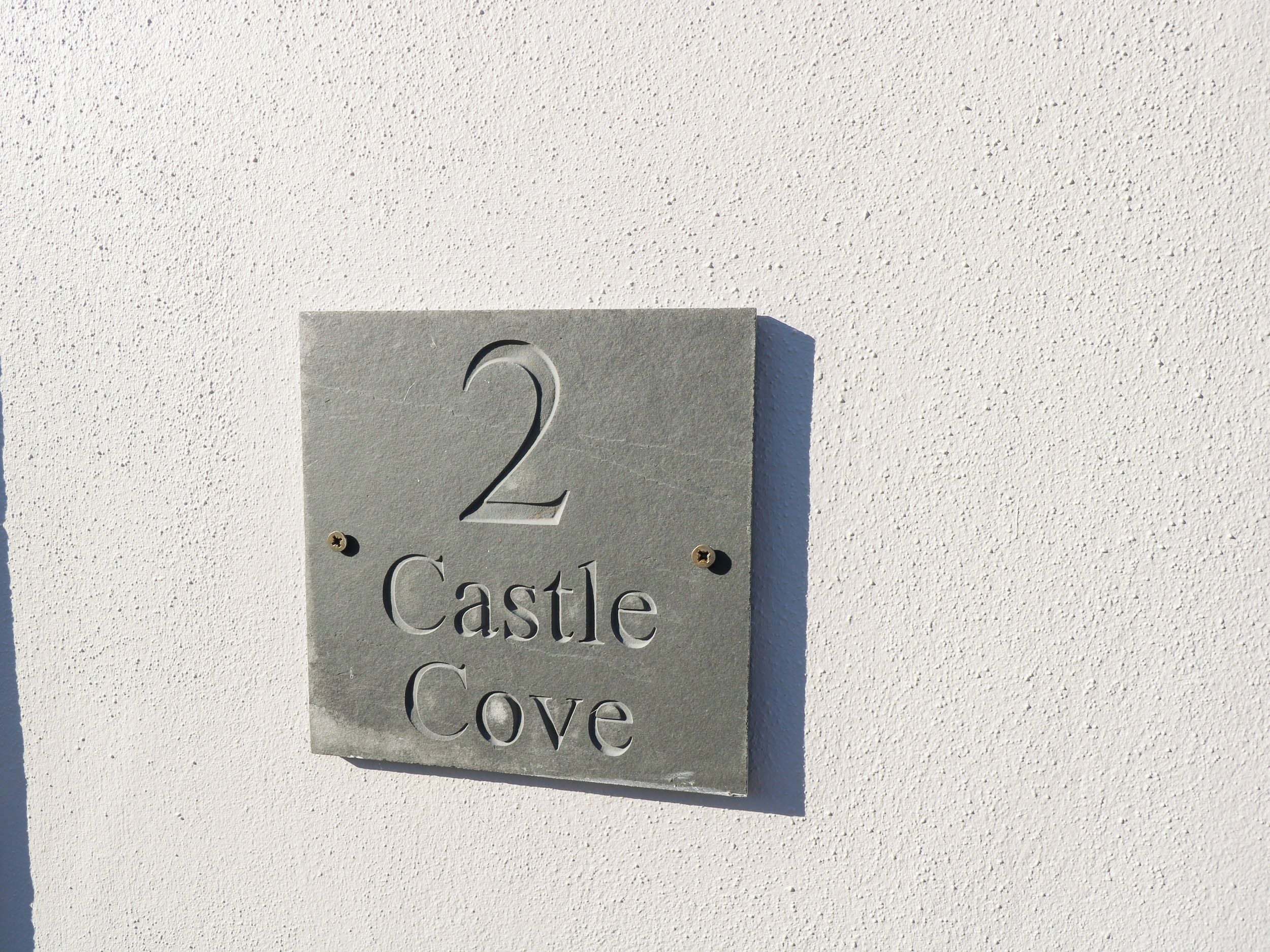 Ein Hausnummernschild mit der Aufschrift '2 Castle Cove' an einer Wand.