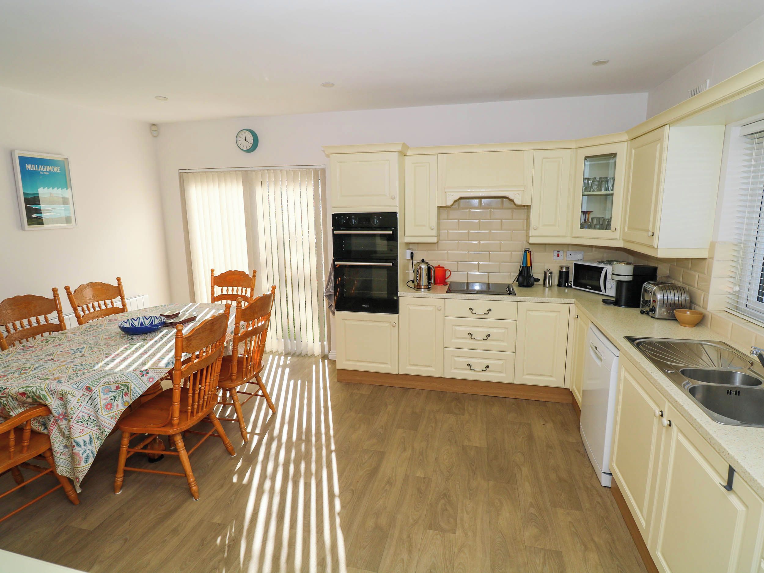 A kitchen with wooden cabinets, a dining table with chairs, and a clock on the wall.