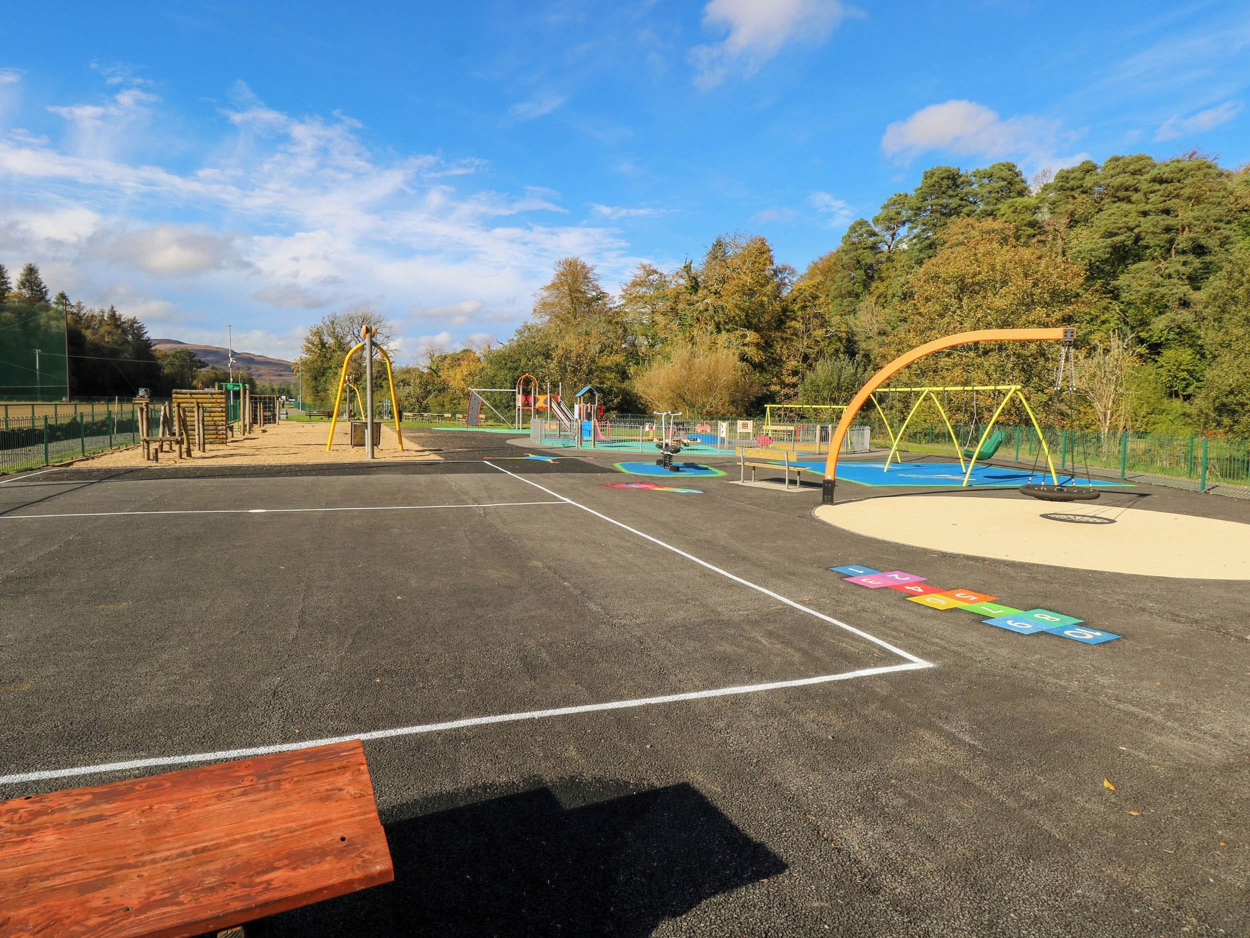 Ein Spielplatz mit verschiedenen Spielgeräten, darunter Schaukeln und Rutschen, umgeben von einem Zaun.