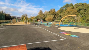 Ein Spielplatz mit verschiedenen Spielgeräten, darunter Schaukeln und Rutschen, umgeben von einem Zaun.