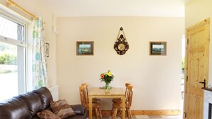 Un salón con un sofá de cuero marrón, una mesa de comedor de madera con cuatro sillas, un florero con flores y un reloj en la pared.