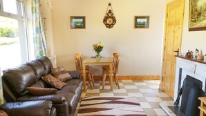 Una sala de estar con un sofá de cuero marrón, una mesa de comedor de madera con dos sillas, un tapete estampado y una chimenea.