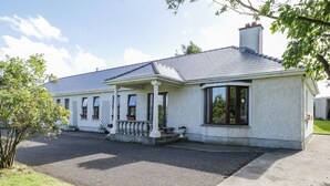 A two-story house with a covered porch, a chimney, and a driveway leading to the front door. - Belladrihid Cottage (Ballysadare)