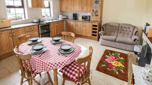 A kitchen with wooden cabinets, a dining table set with plates, a sofa, and a decorative rug. - Belladrihid Cottage (Ballysadare)