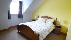 Een slaapkamer met een schuine plafond, een houten bed, twee nachtkastjes met lampen, en een raam met gordijnen.