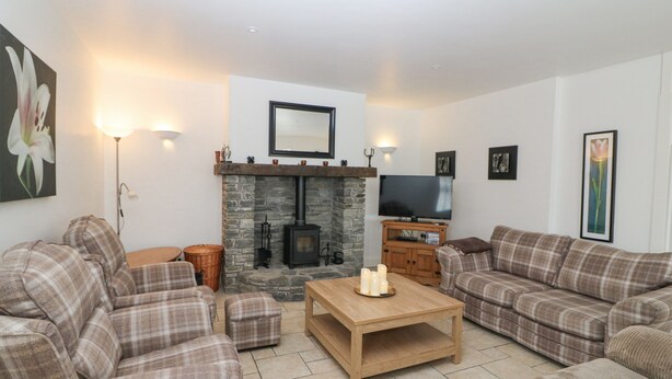 A living room with a stone fireplace, a television, and plaid furniture. - Rock Lawn Cottage (Drimoleague)