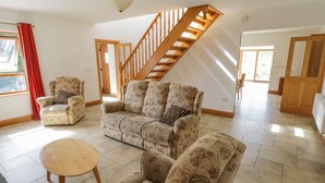 A spacious living room with a wooden staircase, a floral sofa, and a round coffee table. - Blue Stack House (Letterbarrow)