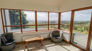 A corner room with large windows, a wooden bench, and two wicker chairs. - Blue Stack House (Letterbarrow)