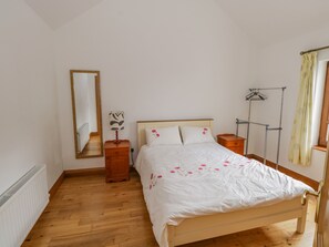 A bedroom with a wooden bed, a nightstand, a mirror, a radiator, and a window with curtains. - Blue Stack House (Letterbarrow)