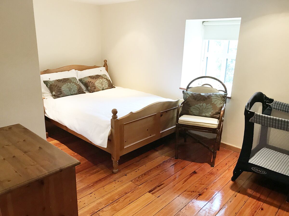 A bedroom with a wooden bed, a chair, a small wooden table, and a window with a view.