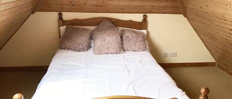 A bedroom with a sloped ceiling, a wooden bed frame, and a white mattress.