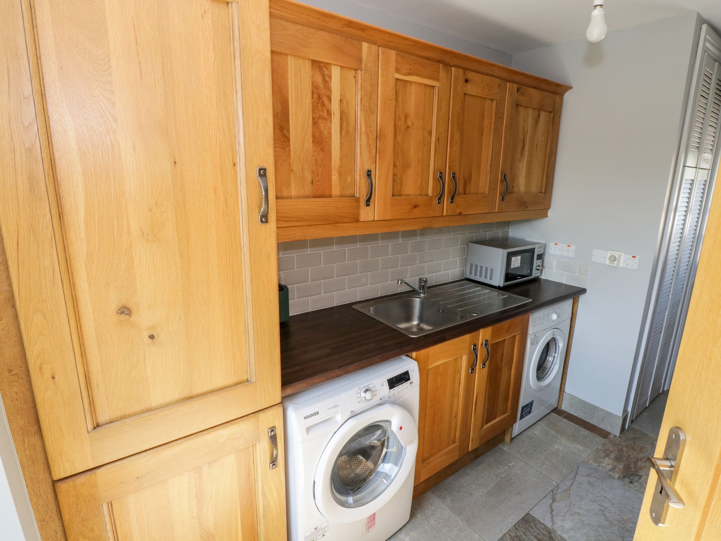 A compact kitchen with wooden cabinets, a built-in microwave, a sink, and a front-loading washing machine.