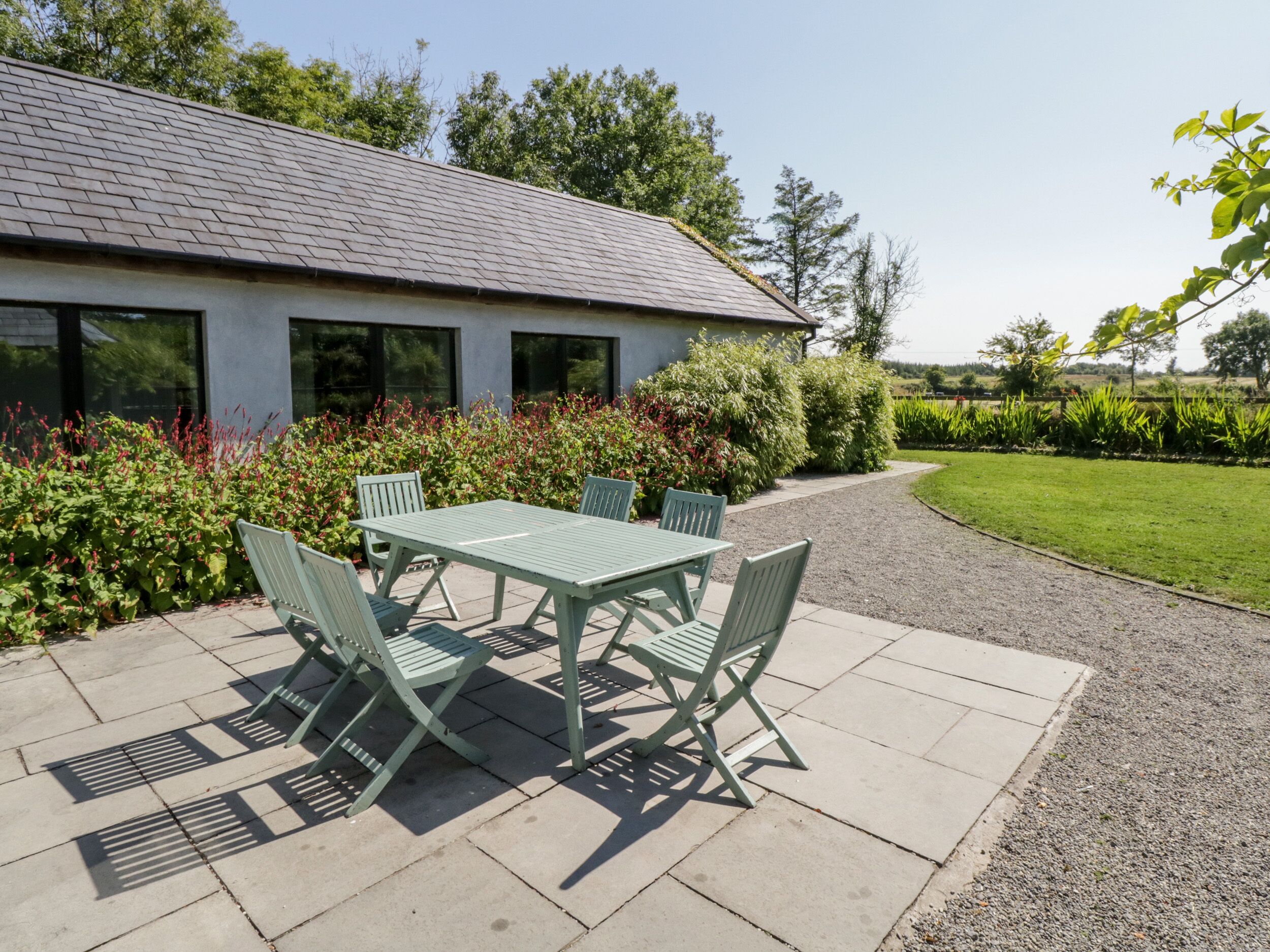 A patio with a table and chairs, a gravel path, and a house with a sloped roof.