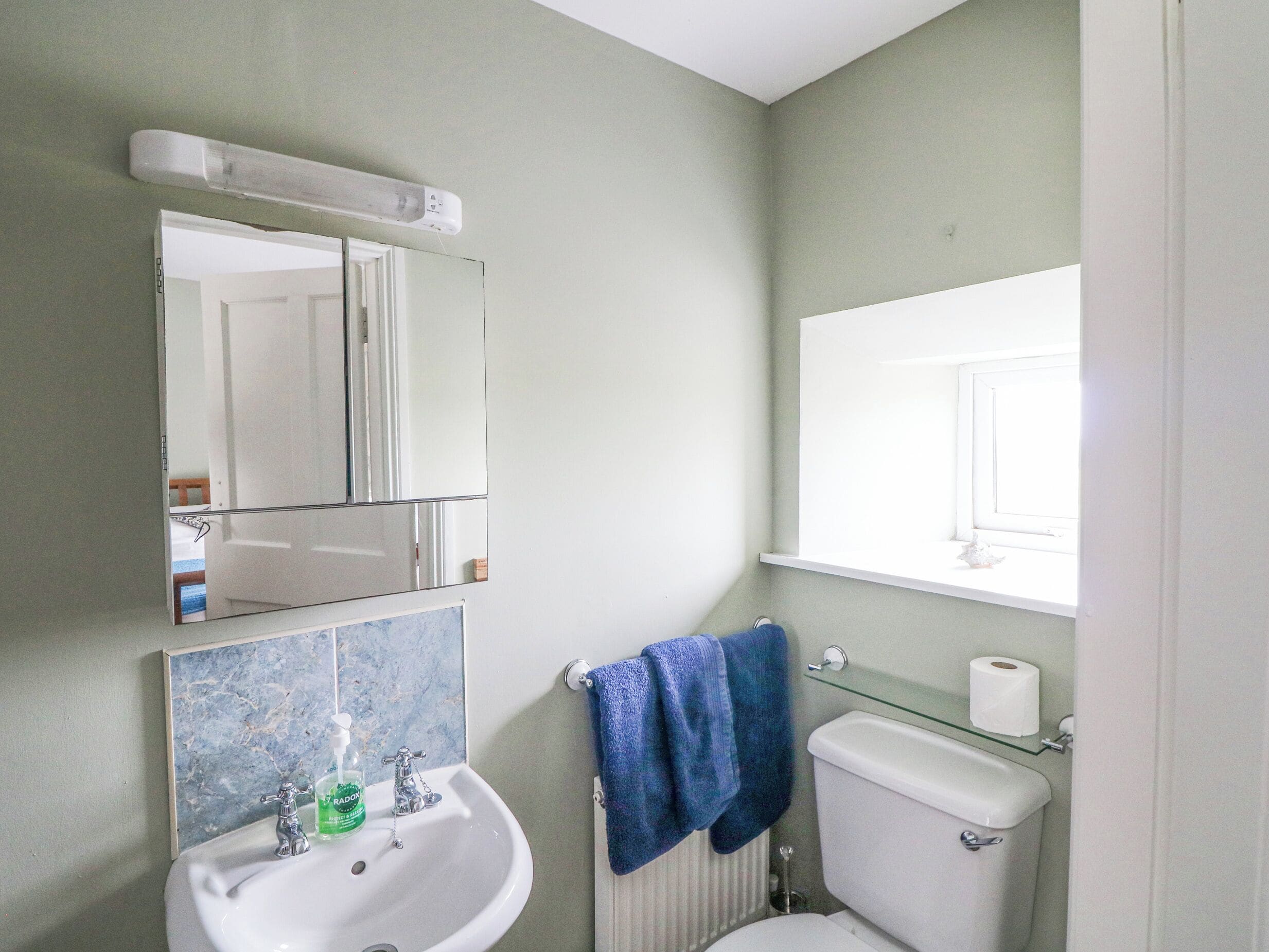Un baño con lavamanos blanco, un espejo, inodoro y ventana.