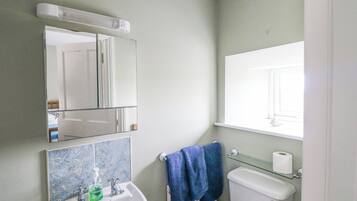 Un baño con lavamanos blanco, un espejo, inodoro y ventana.