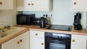 A compact kitchen with white cabinets, a microwave, a toaster, and a stove.