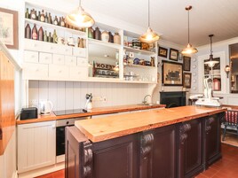 A kitchen with wooden cabinets, a central island, pendant lighting, and shelves with various kitchen items.