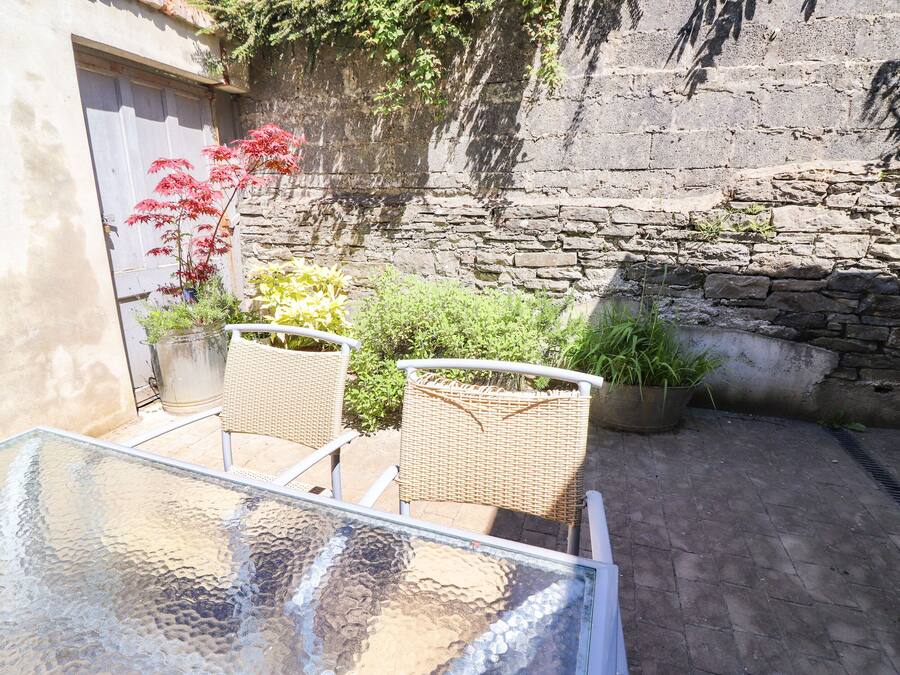 A glass table with wicker chairs in a courtyard with stone walls and potted plants.