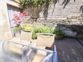 Una mesa de vidrio con sillas de mimbre en un patio con muros de piedra y plantas en macetas.